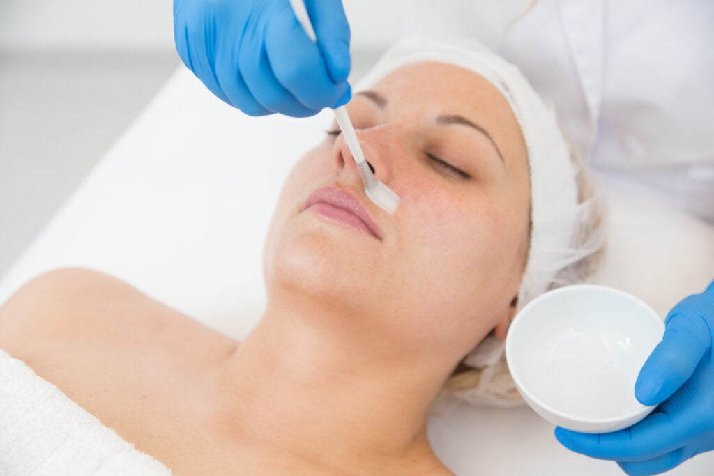 Aesthetician applying a chemical peel on female patient's skin