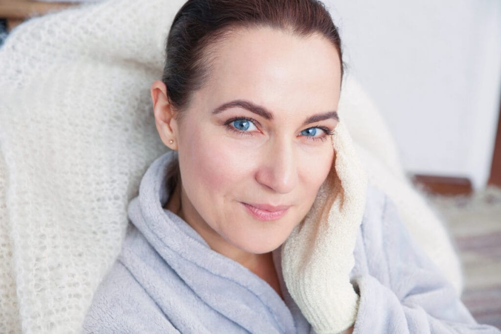 Mature woman with blue eyes touching cheeks and smiling at camera