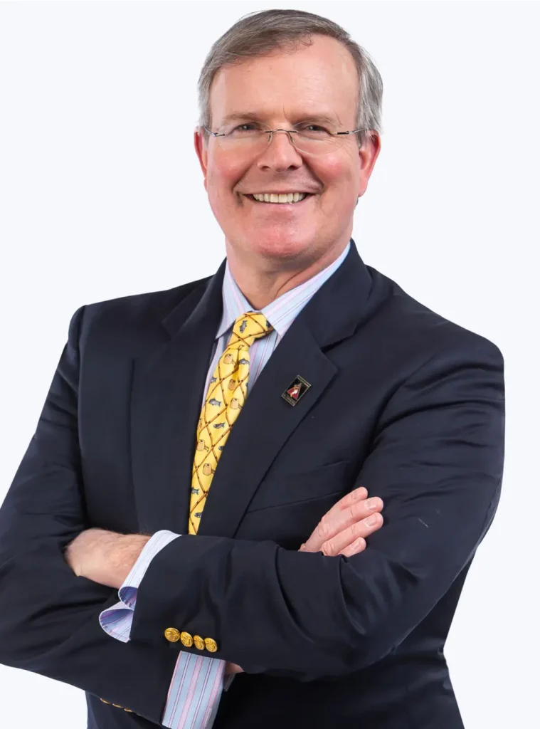 Portrait of Dr. R. Brannon Claytor smiling, with arms crossed, wearing a dark blue suit and yellow tie